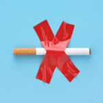 Crossed out cigarette, glued with red adhesive tape to a blue background. No smoking concept.